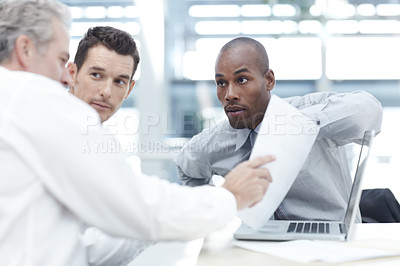 Buy stock photo Three businessmen looking over contracts while sitting down in a meeting