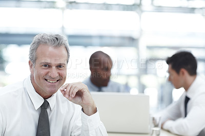 Buy stock photo Portrait of a mature businessman smiling while sitting in front of two younger colleagues