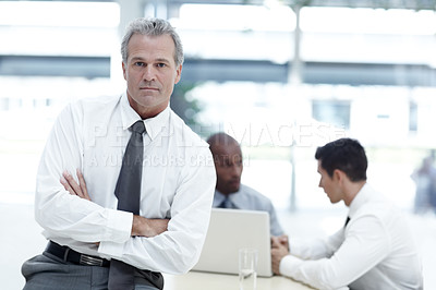Buy stock photo Portrait of a mature businessman sitting with his arms folded in front of two younger colleagues