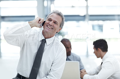 Buy stock photo A mature businessman talking on his cellphone in front of two younger colleagues