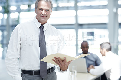 Buy stock photo Portrait of a mature businessman looking through a file in front of two younger colleagues