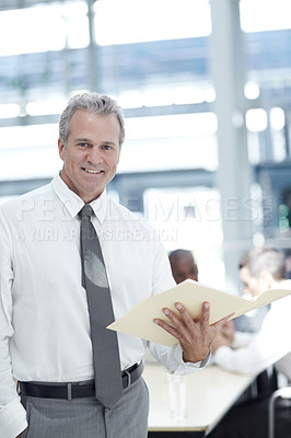 Buy stock photo Portrait of a mature businessman standing with an open file infront of two younger colleagues