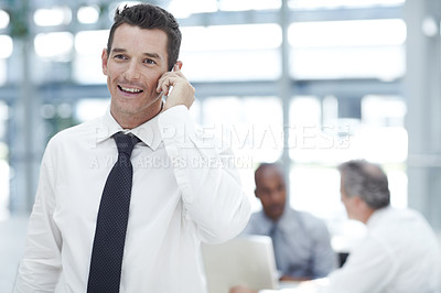 Buy stock photo A young businessman talking on his mobile phone infront of two colleagues