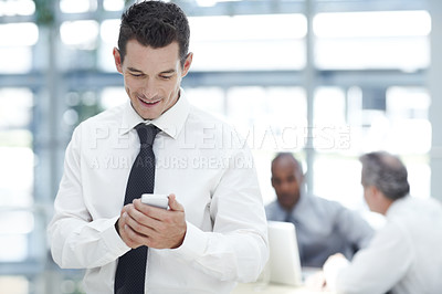 Buy stock photo A young businessman texting on his cellphone in front of two colleagues