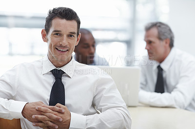 Buy stock photo A handsome businessman sitting at a table and smiling with colleagues in the background