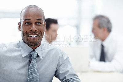 Buy stock photo A handsome businessman looking at the camera and smiling with colleagues working in the background