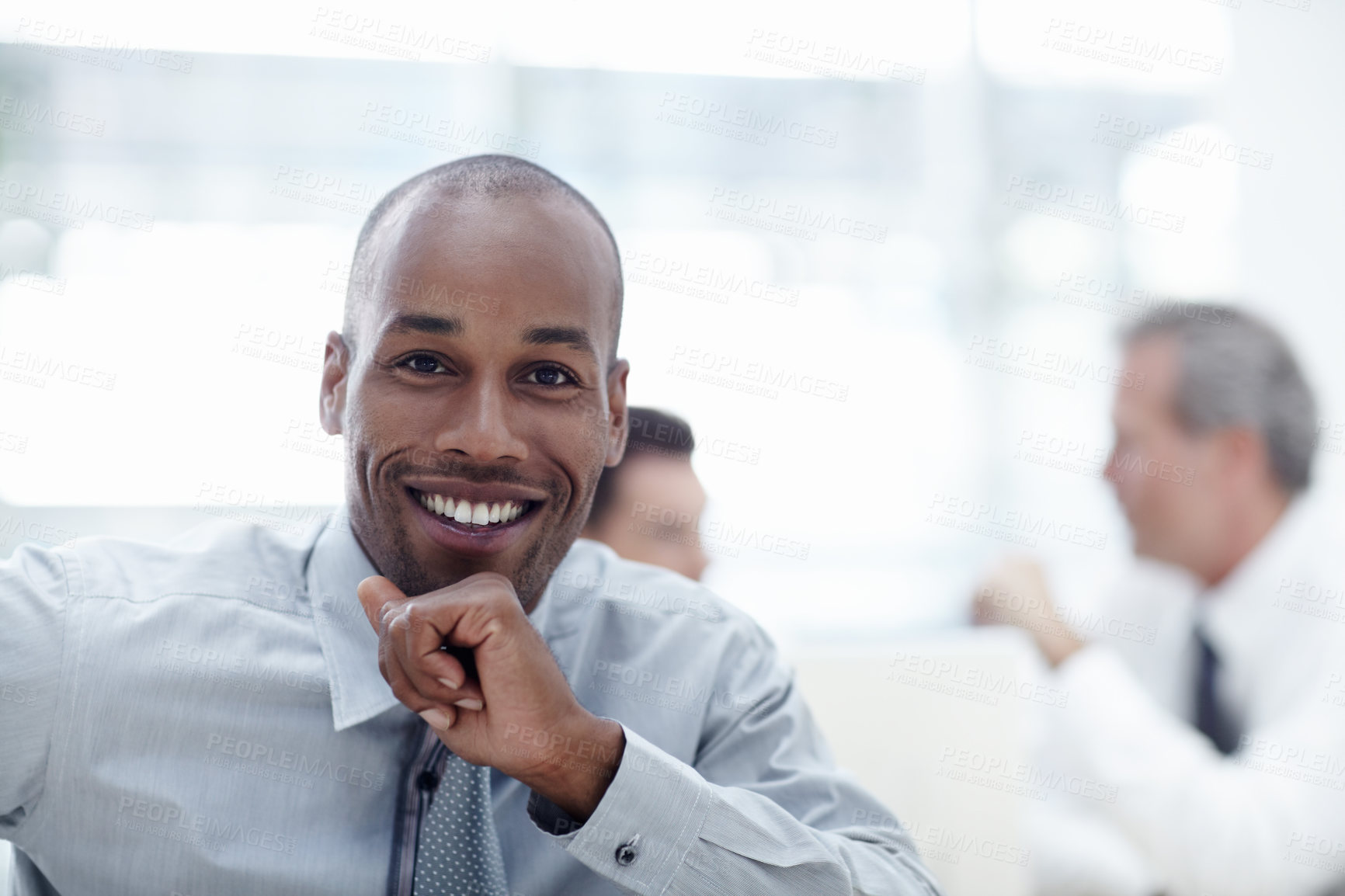 Buy stock photo A handsome African businessman resting his chin on his hand and smiling with colleagues in the background