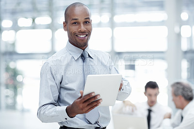 Buy stock photo Handsom African businessman holding a touchpad, smiling and looking at the camera with colleagues working in the background