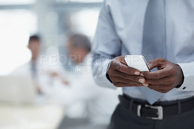 Buy stock photo A close-up of an African businessman's hands holding a cellphone with colleagues working in the background