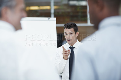 Buy stock photo A handsome businessman stands in front of a flipchart pointing in the direction of colleagues in the foreground