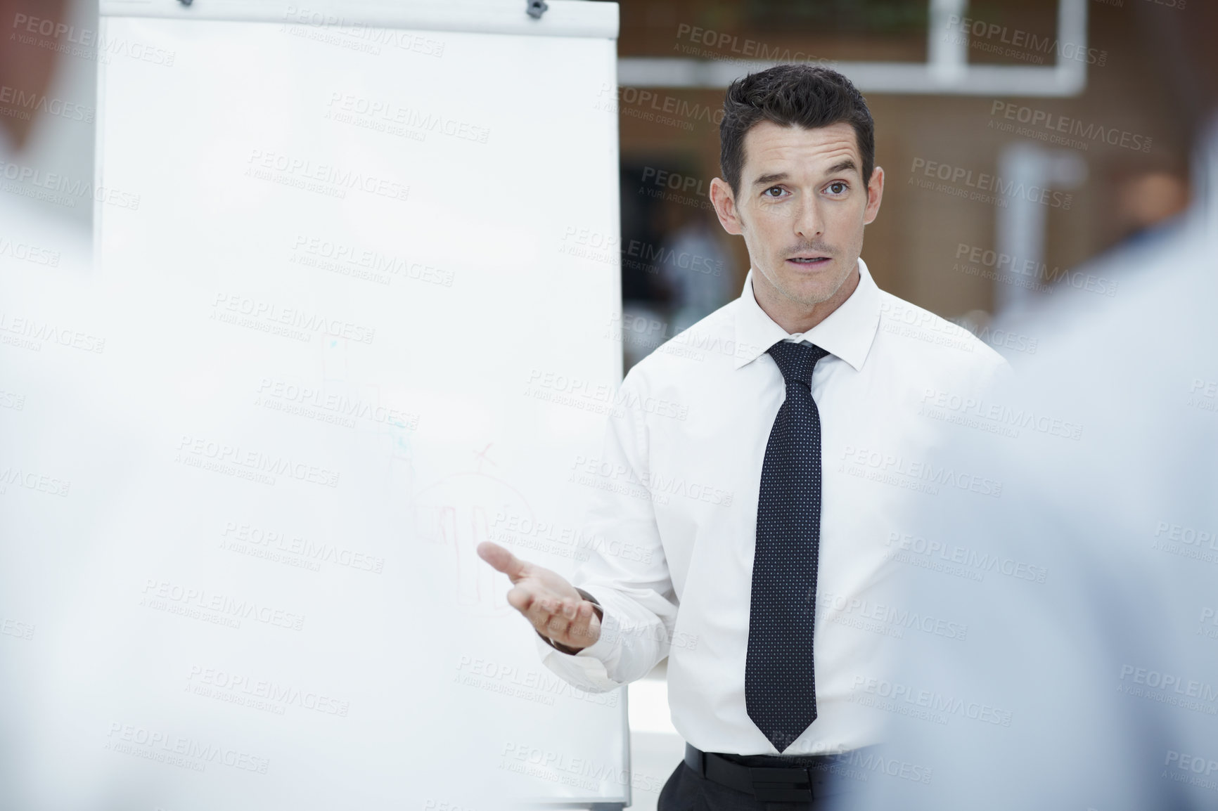 Buy stock photo Handsome businessman standing next to a flipchart talking to his colleagues in the foreground