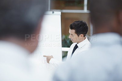 Buy stock photo A businessman point at a flipchart while his colleagues watch in the foreground