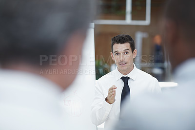 Buy stock photo A handsome businessman stands besides a flipchart and talks to his colleagues in the foreground