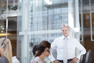 Buy stock photo Shot of a stern looking businessman standing over his team of customer service representatives