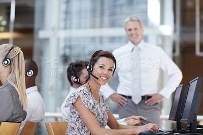 Buy stock photo A beautiful customer service representative sitting at her computer and smiling with coworkers and manager in the background