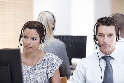 Buy stock photo Two customer service representatives working with colleagues in the background