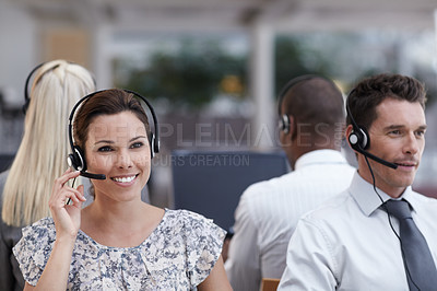 Buy stock photo A beautiful customer service representative taking a call with colleagues working in the background