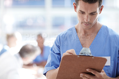 Buy stock photo A medical professional writing on a clipboard with colleagues sitting in the background