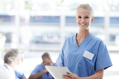 Buy stock photo Medical professional standing and using a touchpad with colleagues sitting in the background