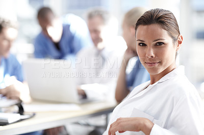 Buy stock photo A beautiful medical professional looks at the camera with colleagues working in the background