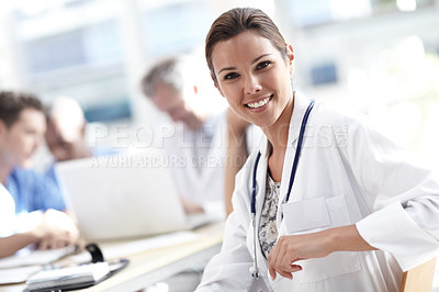 Buy stock photo A beautiful medical professional smiles at the camera with colleagues working in the background