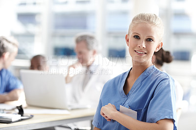 Buy stock photo A beautiful medical professional looks at the camera with colleagues working in the background