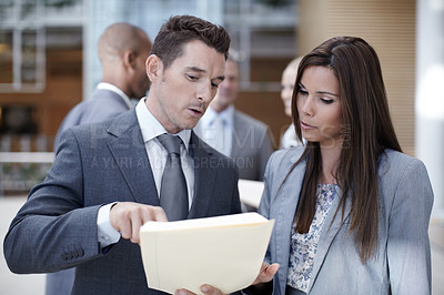 Buy stock photo Two coworkers looking over paperwork together while looking serious