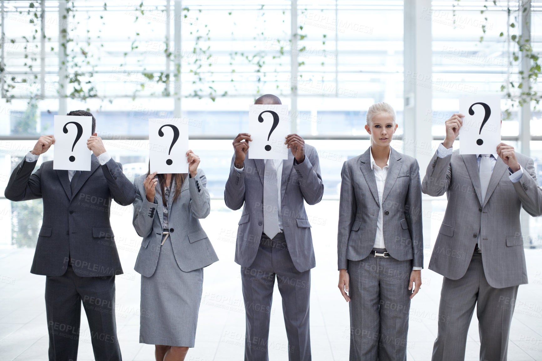 Buy stock photo Concept shot of a young businesswoman looking at the camera while her colleagues hold up question mark signs in front of their faces