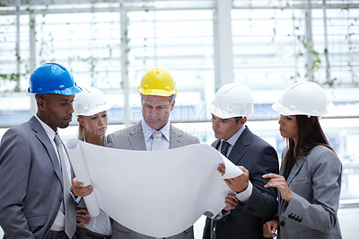 Buy stock photo A diverse group of serious-looking architects looking over blueprints together