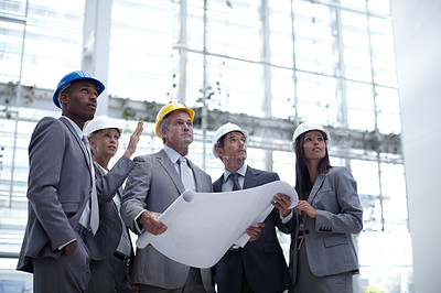 Buy stock photo A low angle shot of a diverse group of architects looking up while holding blueprints 