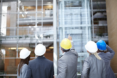 Buy stock photo A rearview shot of a diverse group of engineering professionals pointing up at a building 
