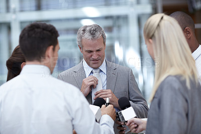 Buy stock photo Shot of a mature businessman adjusting his tie while being interviewed by reporters
