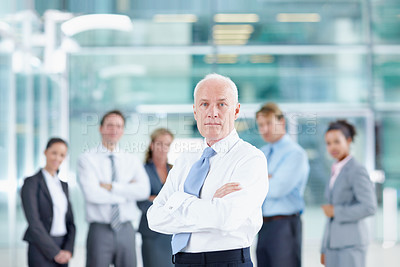 Buy stock photo Serious senior businessman standing with his team in the background - portrait 