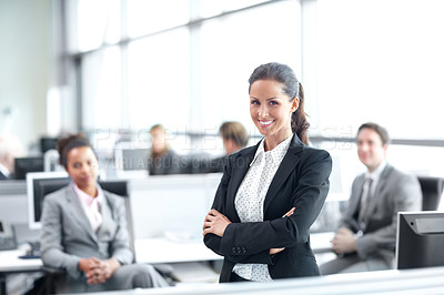 Buy stock photo Pretty young businesswoman standing confidently in the office with her coworkers behind her - portrait