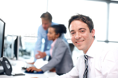 Buy stock photo Smiling businessman sitting at his desk with his colleagues working in the background - portrait 