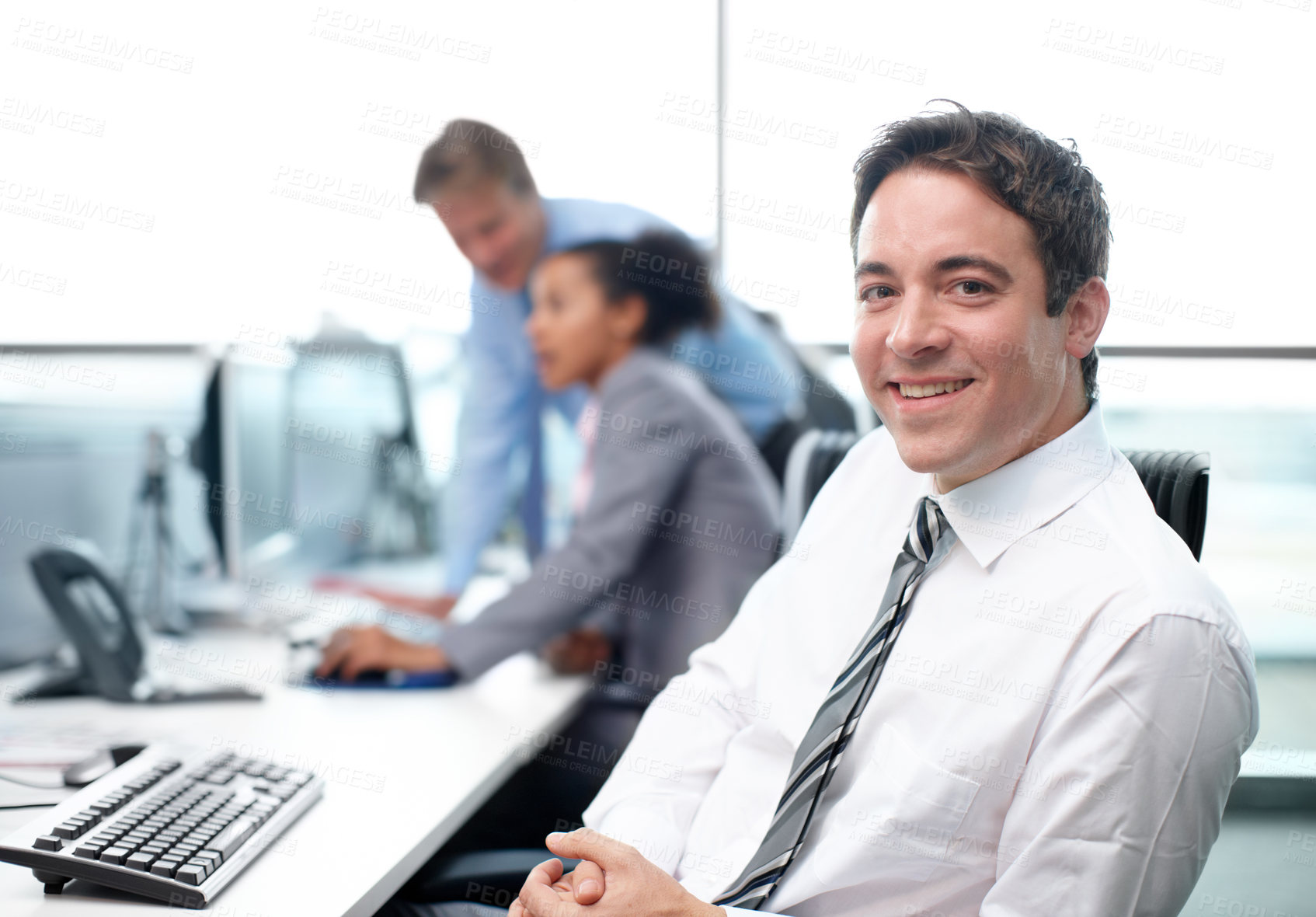 Buy stock photo Confident businessman sitting at his desk with his colleagues working in the background - portrait 
