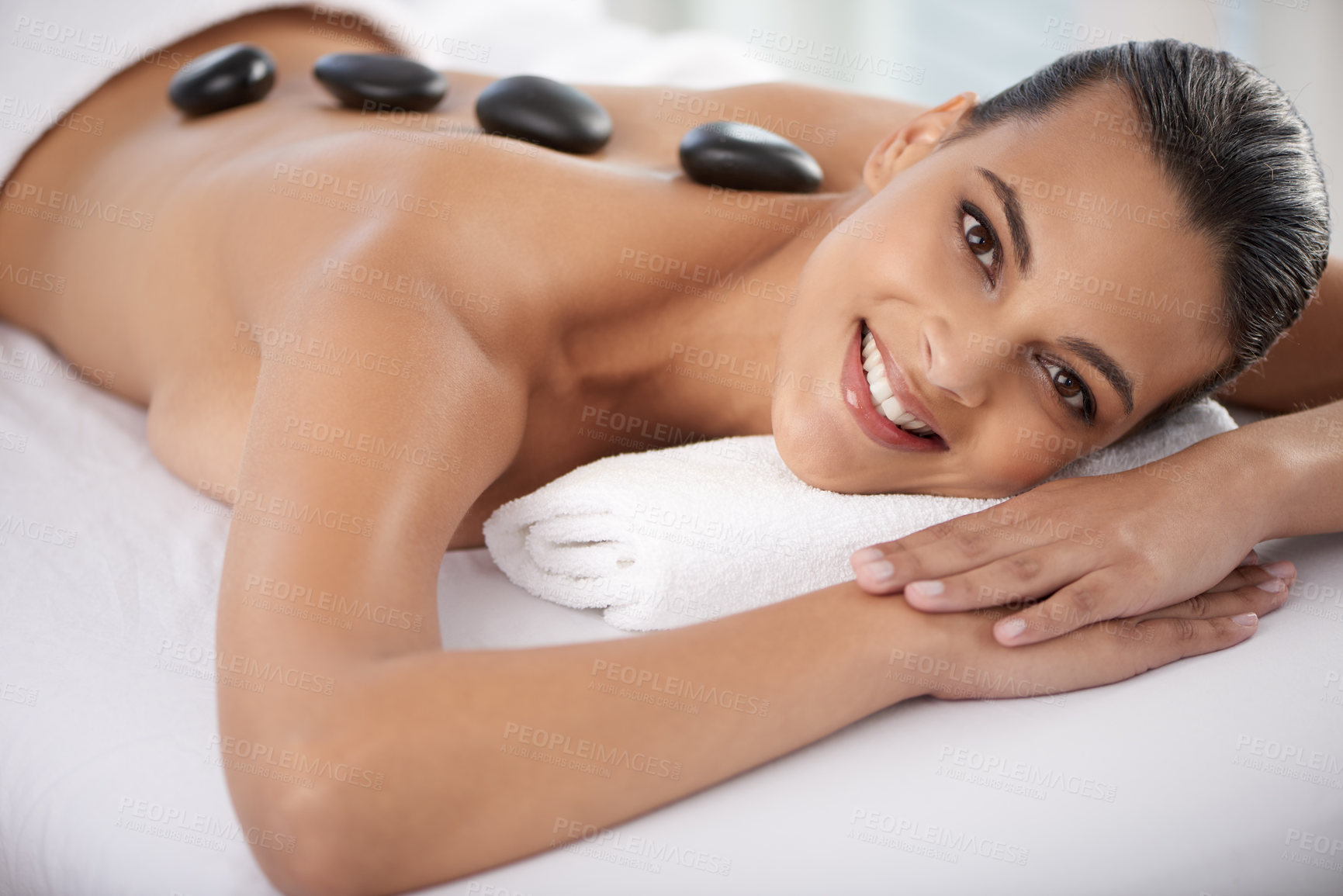 Buy stock photo Relax, hot stone and portrait of woman with massage at spa for wellness, health and back treatment. Self care, smile and young female person with cosmetic warm stone back therapy at beauty salon.