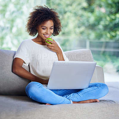 Buy stock photo Shot of a young woman eating an apple while using her laptop at home