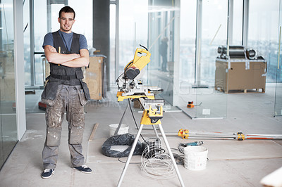 Buy stock photo Portrait of one happy young contractor standing with arms crossed working on industrial architecture project at construction site. Engineer builder using power saw equipment tools to renovate building