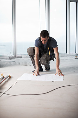 Buy stock photo Young contractor checking his plans on a construction site indoors