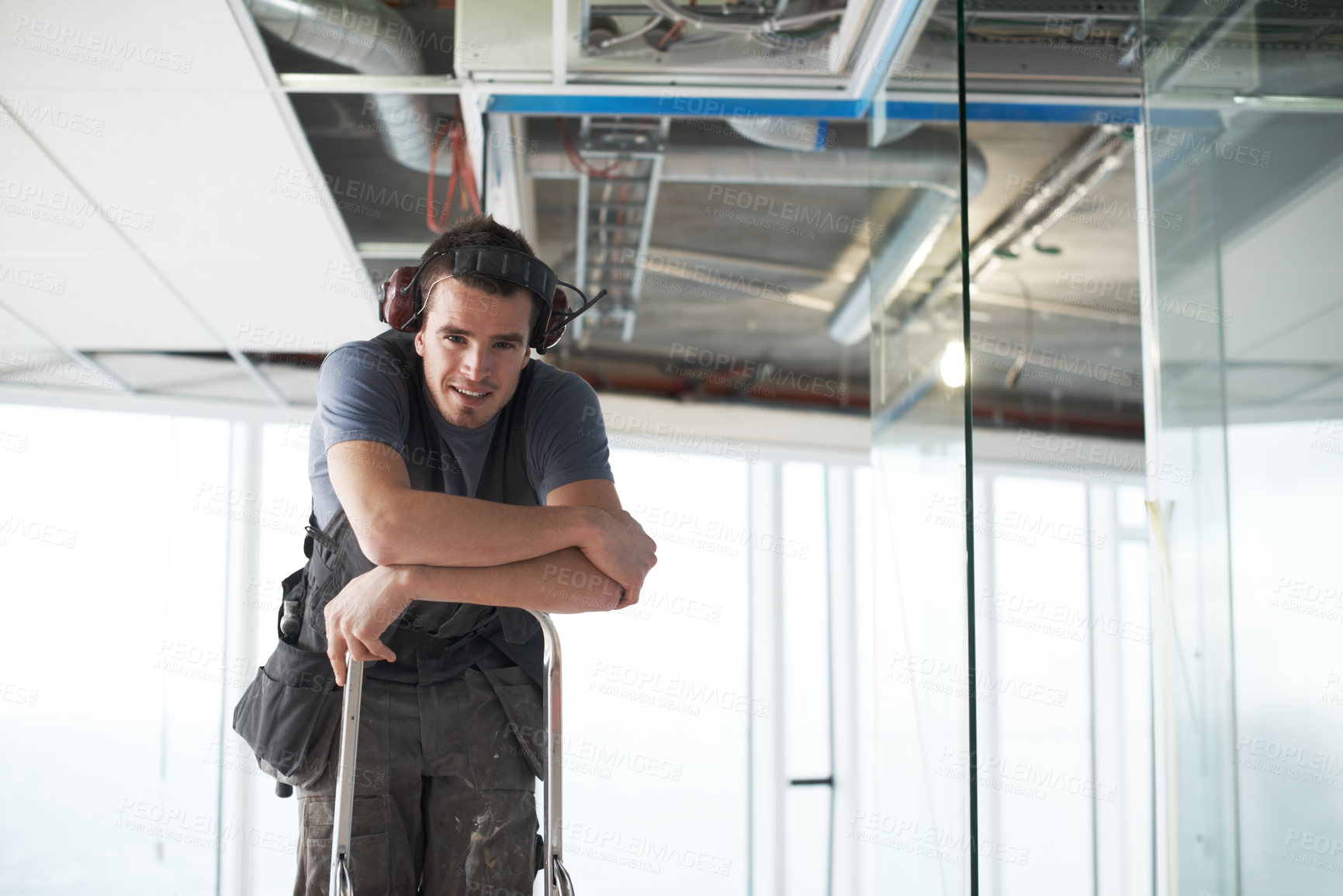 Buy stock photo Portrait of one happy young building contractor wearing noise cancelling headphone earmuffs climbing ladder for industrial architecture project at construction site. Engineer renovating property roof