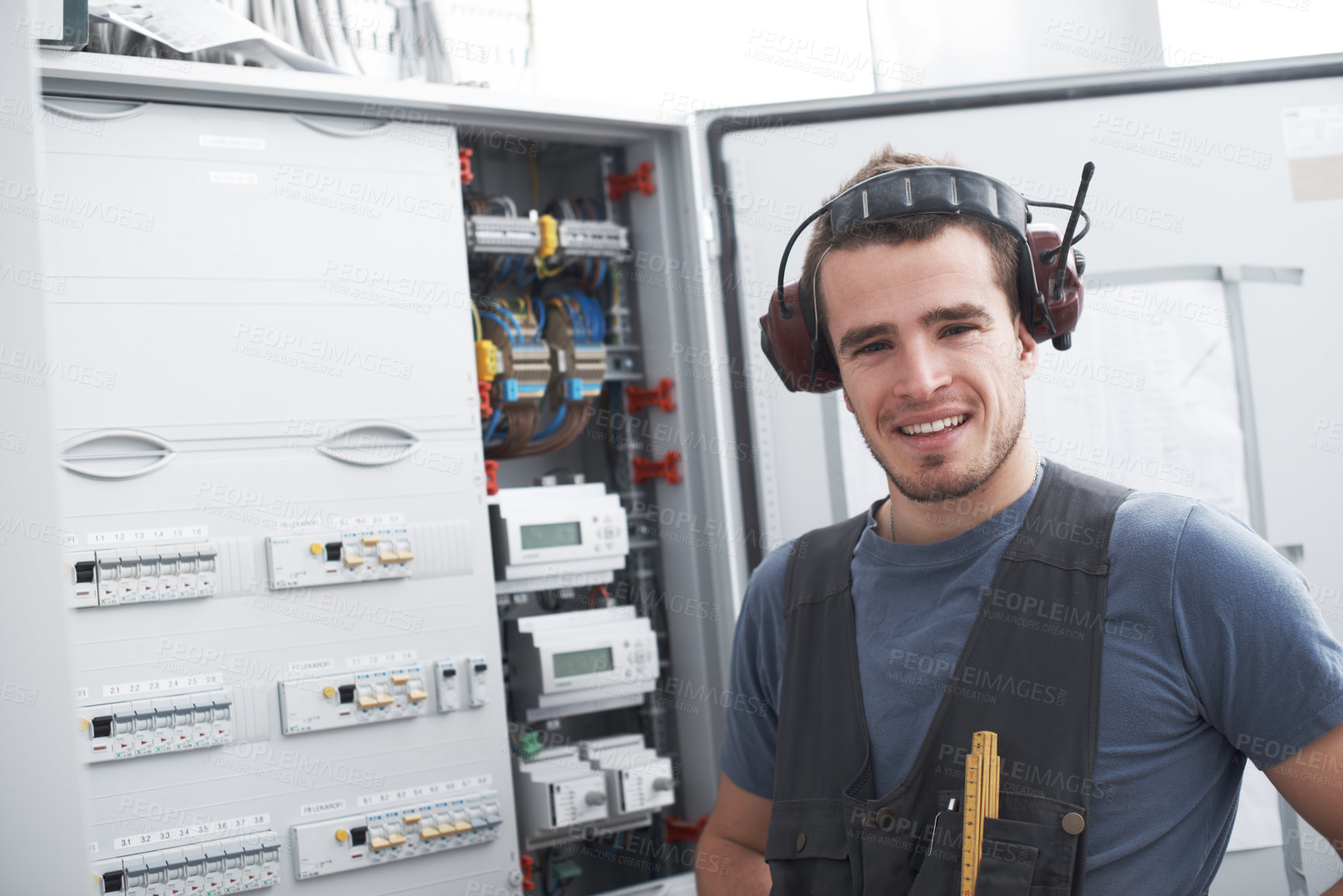 Buy stock photo Young contractor standing alongside an electrical distribution board