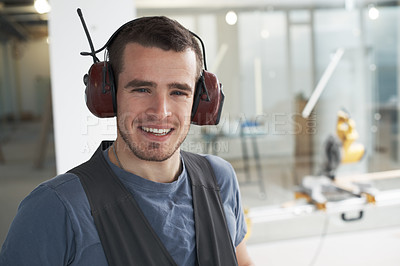 Buy stock photo Portrait of one happy young contractor wearing nose cancelling headphone earmuffs while working on industrial architecture project at construction site. Engineer and builder renovating property