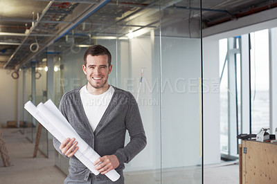 Buy stock photo Young architect standing in a building and holding his plans with a smile