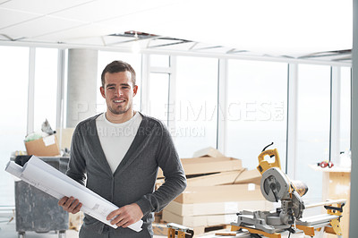 Buy stock photo Young architect standing in a building and holding his plans with a smile