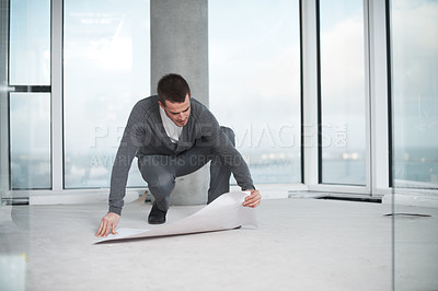 Buy stock photo Young architect checking his plans while crouching in an empty room