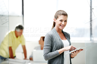 Buy stock photo A young female architect standing and using a digital tablet with some of her colleagues in the background