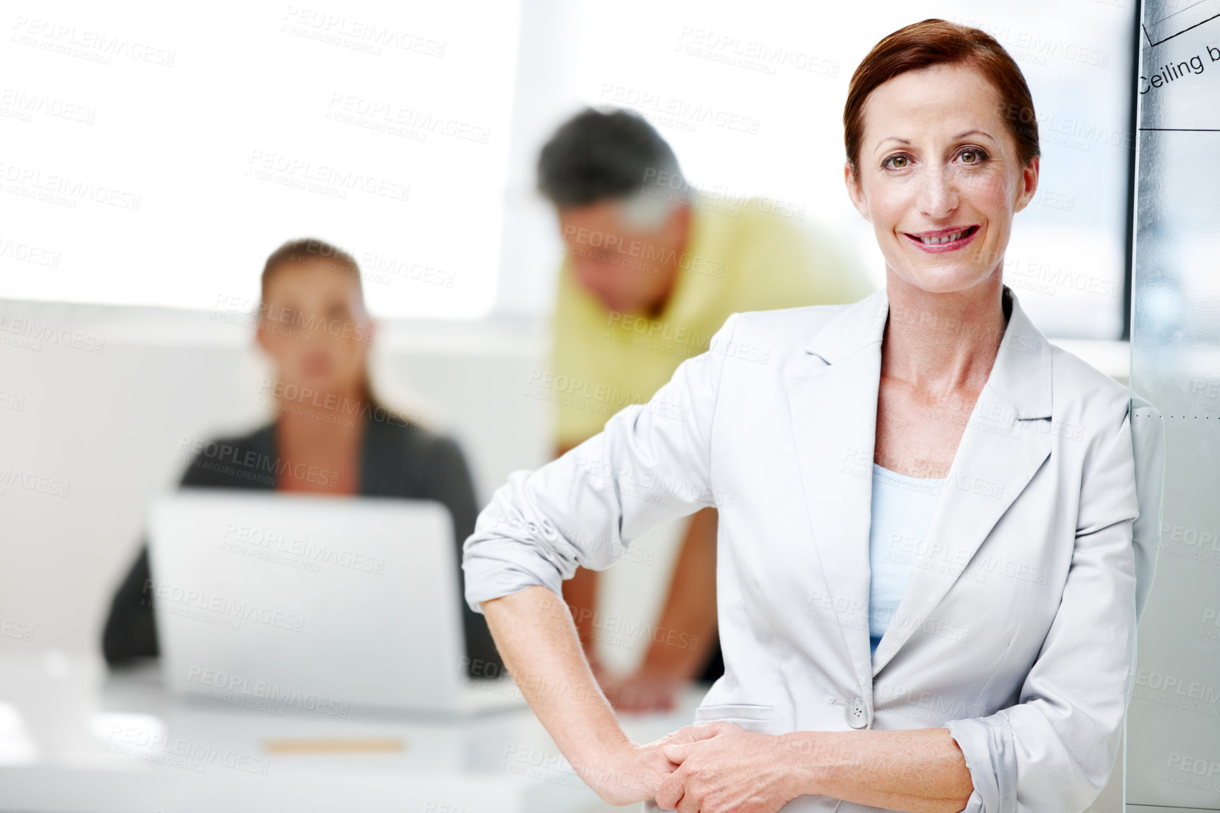 Buy stock photo A mature female architect standing confidently with her colleagues in the background