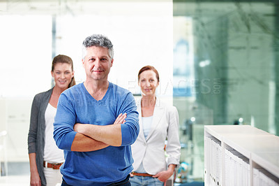 Buy stock photo An mature businessman standing confidently with his co-workers behind him