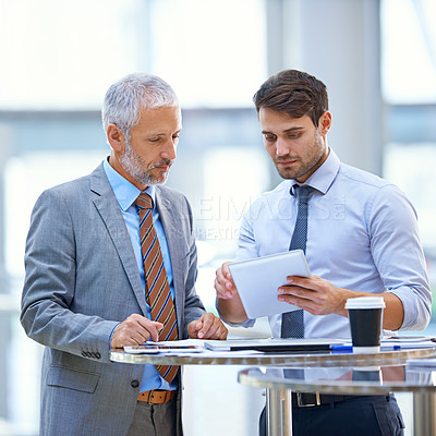 Buy stock photo Shot of a young businessman with a tablet discussing work with his colleague